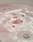 Pink bath bomb with rose petals in a bathtub filled with bubbles
