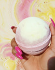 Bath bomb held in a hand with labels indicating ingredients on a colorful background