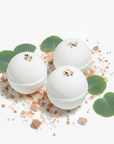 Three eucalyptus-scented bath bombs with eucalyptus leaves on a white surface.