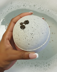 Hand holding a textured bath bomb over a bathtub filled with bubbles