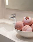 Rose pink bath bomb in a white bowl on a bathroom counter.